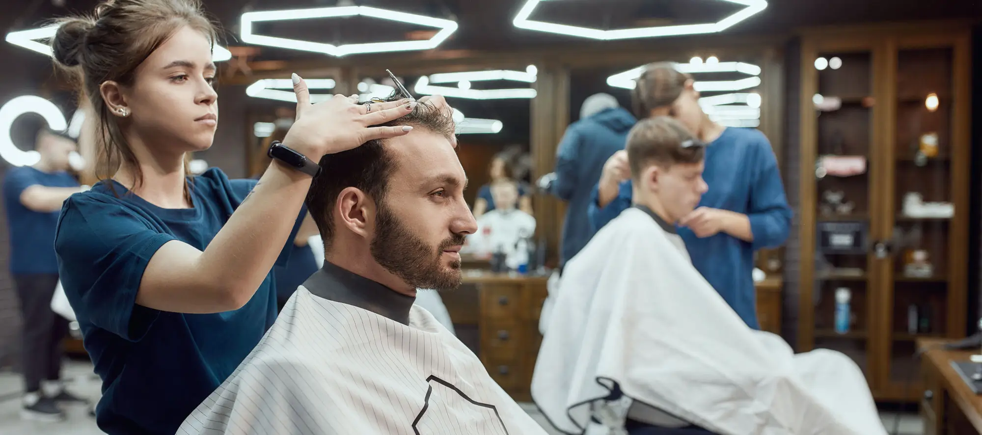 Side view of a professional barber girl making new modern haircut for a young bearded man.
