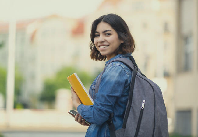 Female student on campus with orange binder.