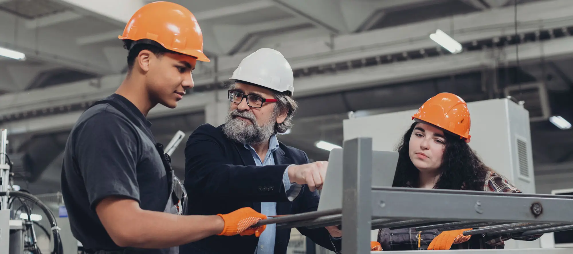 Experienced engineer guiding young manufacturing apprentices in factory