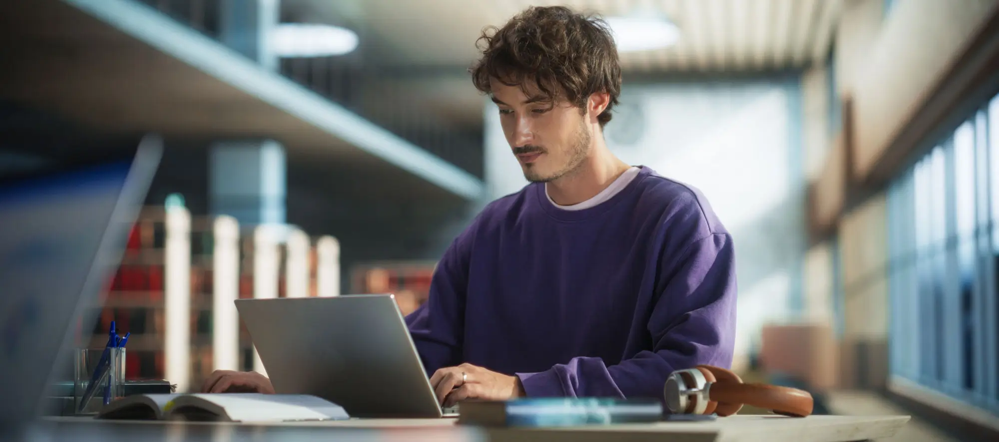 Male student in library typing on a laptop at a desk.