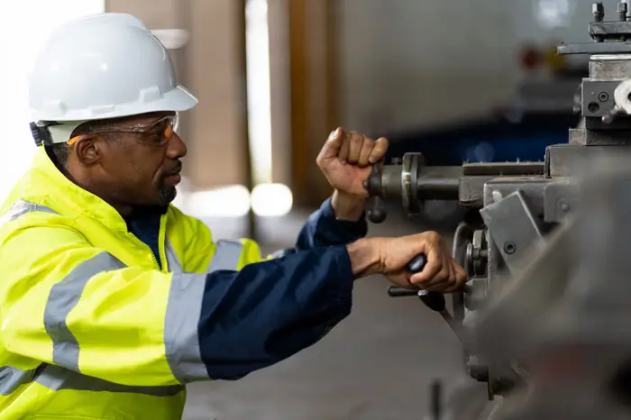 Black male worker working with heavy machine with safety uniform, goggles and helmet.