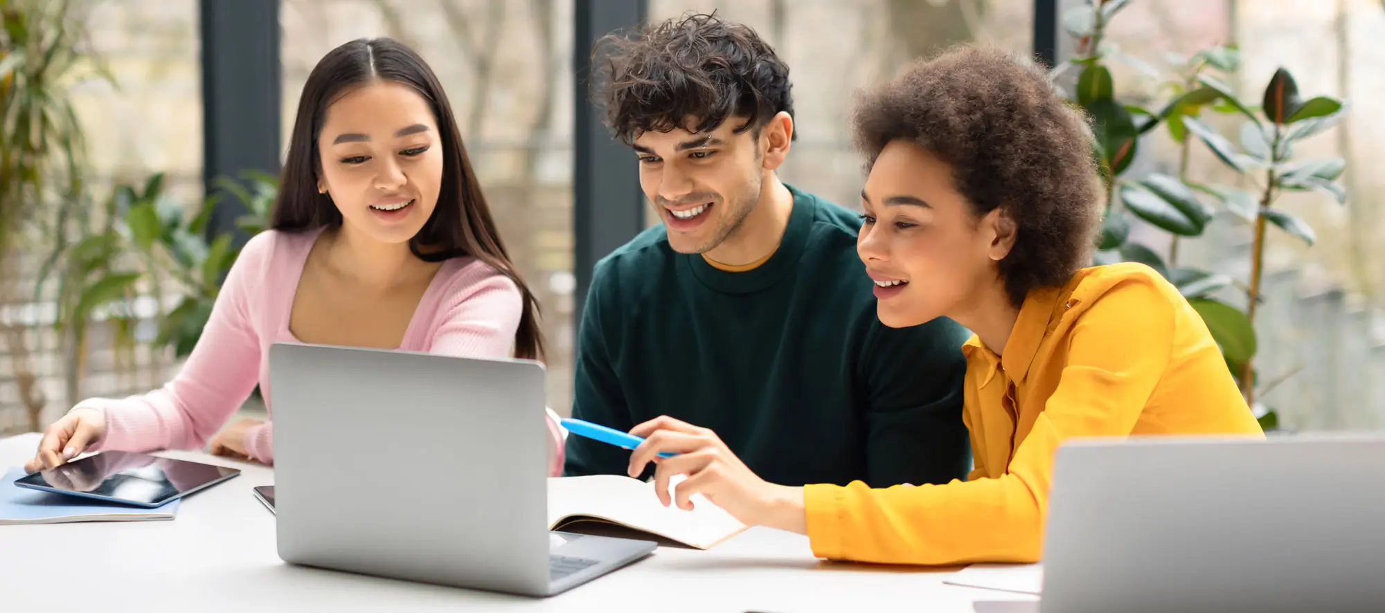 Happy international students friends sitting at desk in coworking space and using laptop