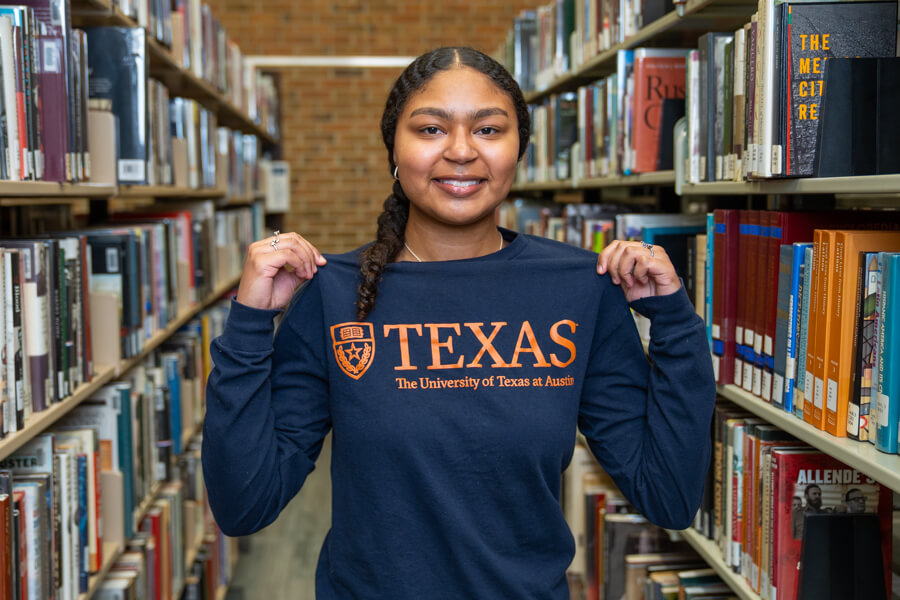 COM Collegiate High School Student Grace Pope Wears a University of Texas at Austin Shirt in the COM Library.