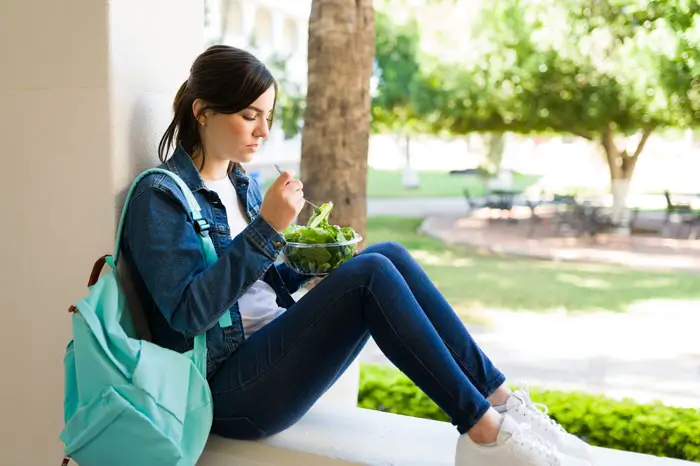 Young female student sitting on campus eating a salad outside