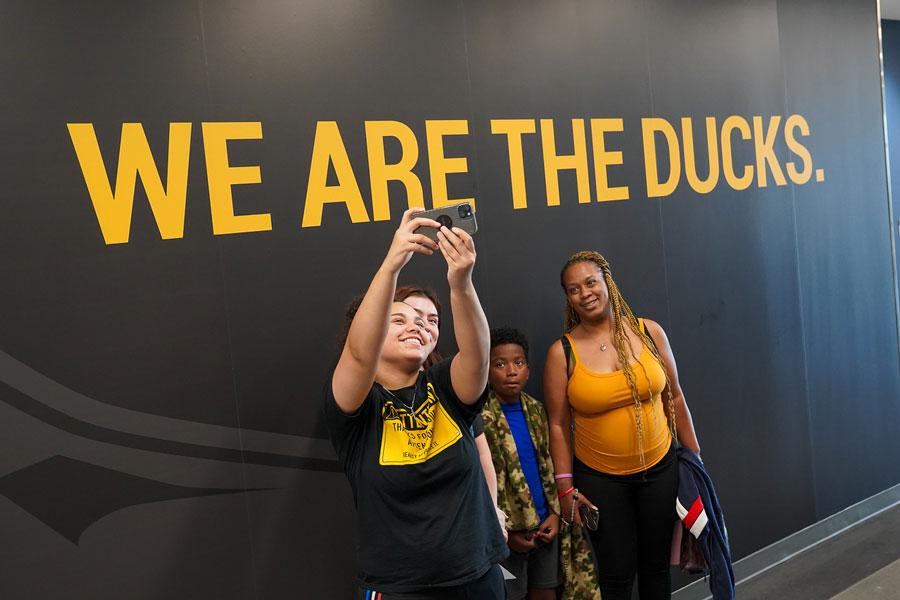 Students taking a seflie in front of a wall that says "We are the Ducks."