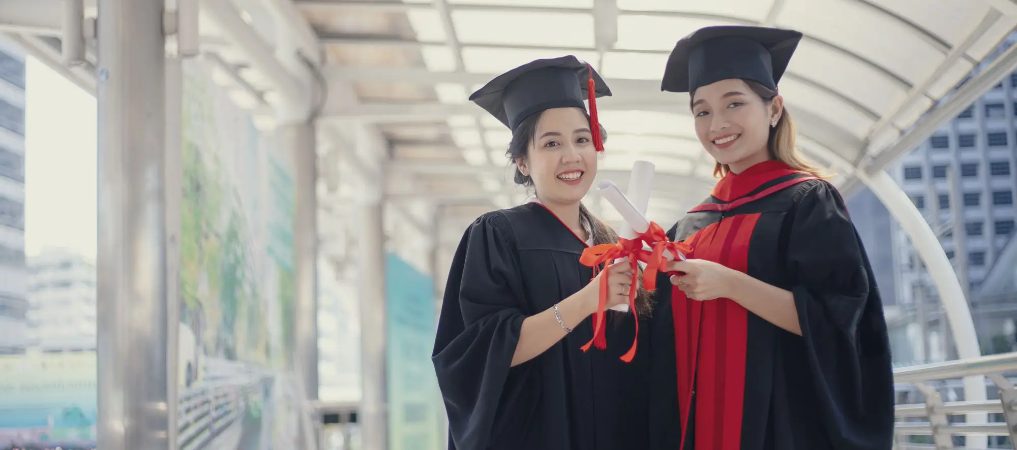 Two graduates holding diplomas in building hallway