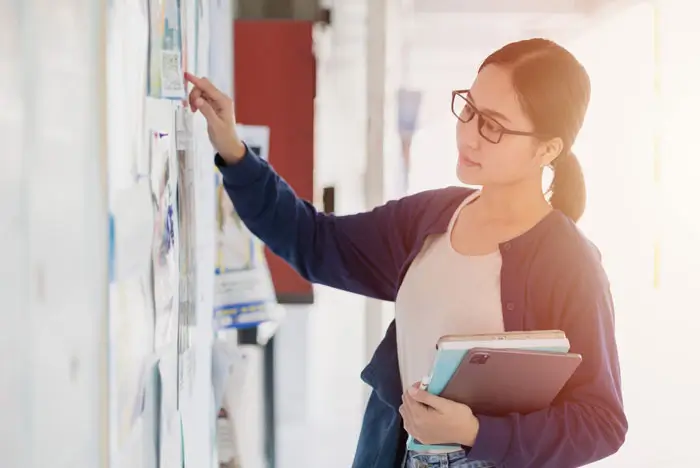 Female student wearing glasses reading flier's on bulletin board.