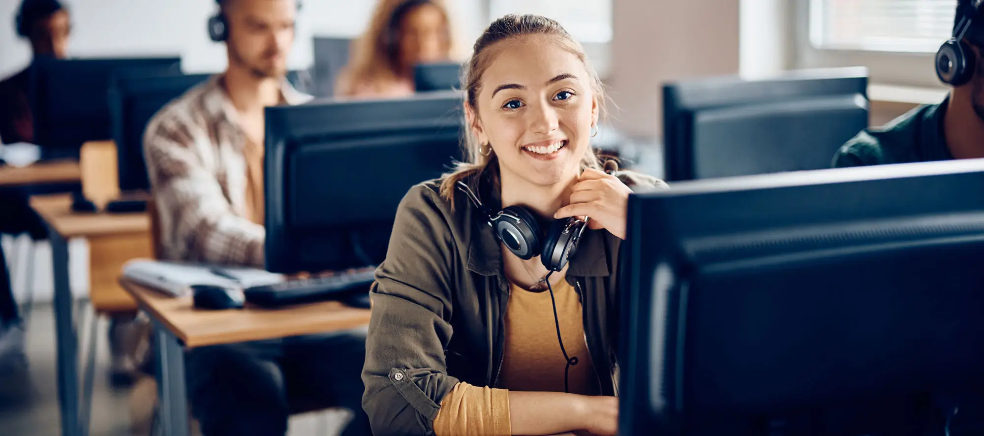 Happy female student using desktop PC during computer class and looking at camera.